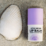 Little Urchin Cherry & Kakadu Plum Lip Balm 4g: the cherry and Kakadu plum lip balm on sand beside a shell.