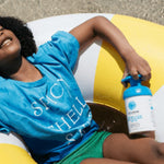 Child relaxing on a colourful inflatable ring at the beach while holding a blue-pump bottle of Little Urchin Clear Zinc Sunscreen SPF50+ 300g.