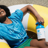 Child relaxing on a colourful inflatable ring at the beach while holding a blue-pump bottle of Little Urchin Clear Zinc Sunscreen SPF50+ 300g.
