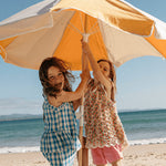 Little Urchin Kids Natural Clear Zinc Sunscreen SPF50+ 100g — two children beneath a yellow beach umbrella.