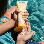 Little Urchin Kids Natural Clear Zinc Sunscreen SPF50+ 100g — hands holding the yellow 100g sunscreen tube beside a swimming pool.