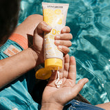 Little Urchin Kids Natural Clear Zinc Sunscreen SPF50+ 100g — hands holding the yellow 100g sunscreen tube beside a swimming pool.