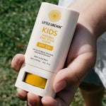 Little Urchin Kids Natural Zinc Stick Clear, SPF 50+  20g — a hand holding the yellow and white kids clear zinc stick outdoors.