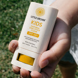 Little Urchin Kids Natural Zinc Stick Clear, SPF 50+  20g — a hand holding the yellow and white kids clear zinc stick outdoors.