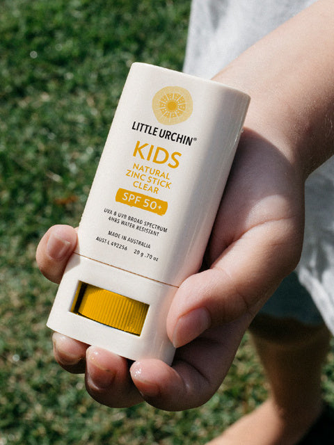 Little Urchin Kids Natural Zinc Stick Clear, SPF 50+  20g — a hand holding the yellow and white kids clear zinc stick outdoors.