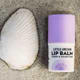 Little Urchin cherry lip balm styled on sand with a shell