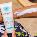 Little Urchin Natural Clear Zinc Sunscreen SPF30 100g — the 100g tube held beside an arm with sunscreen spread across the skin.