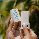 Little Urchin Natural Zinc Stick Clear SPF 50+ 20g — hands holding the clear zinc stick and its cap beneath palm trees.