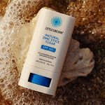 Little Urchin Natural Zinc Stick Clear SPF 50+ 20g — the clear zinc stick lying beside seashells and sea foam.