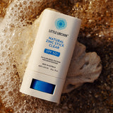 Little Urchin Natural Zinc Stick Clear SPF 50+ 20g — the clear zinc stick lying beside seashells and sea foam.