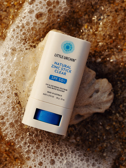 Little Urchin Natural Zinc Stick Clear SPF 50+ 20g — the clear zinc stick lying beside seashells and sea foam.