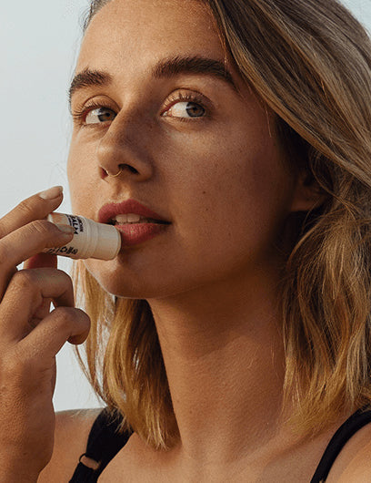 Little Urchin Tropical Pawpaw Lip Balm 4g: a woman applying the tropical pawpaw lip balm to her lips.