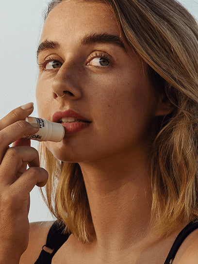 Little Urchin Tropical Pawpaw Lip Balm 4g: a woman applying the tropical pawpaw lip balm to her lips.