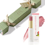Soft Buttery Pinks Bon Bon: light green Christmas cracker with gold ribbons, Guava Blush Lip Nourish lipstick, its white carton and a soft pink colour smear.