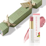 Soft Buttery Pinks Bon Bon: light green Christmas cracker with gold ribbons, Guava Blush Lip Nourish lipstick, its white carton and a soft pink colour smear.
