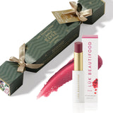 A Flush of Rose Bon Bon: dark green Christmas cracker with gold ribbons, Rosé Lip Nourish lipstick, its white carton and a wine-red colour smear.