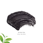 Black Tea Lash Nourish Mascara swatch showing a thick, textured stroke of deep inky black mascara, with green tea leaves in the corner.