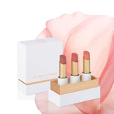 Perfect Nudes Lip Nourish Trio with Tea Rose, Nude Pink and Peach Melon lipsticks in an open white and gold gift box, with its lid and a large pink petal behind.