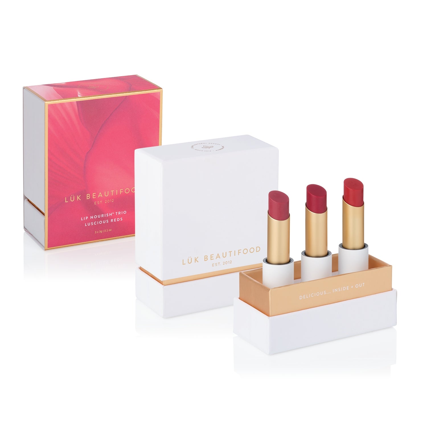 Luscious Reds Lip Nourish Trio with three uncapped red-toned lipsticks in an open white and gold box, beside the white lid and pink-and-gold outer sleeve.