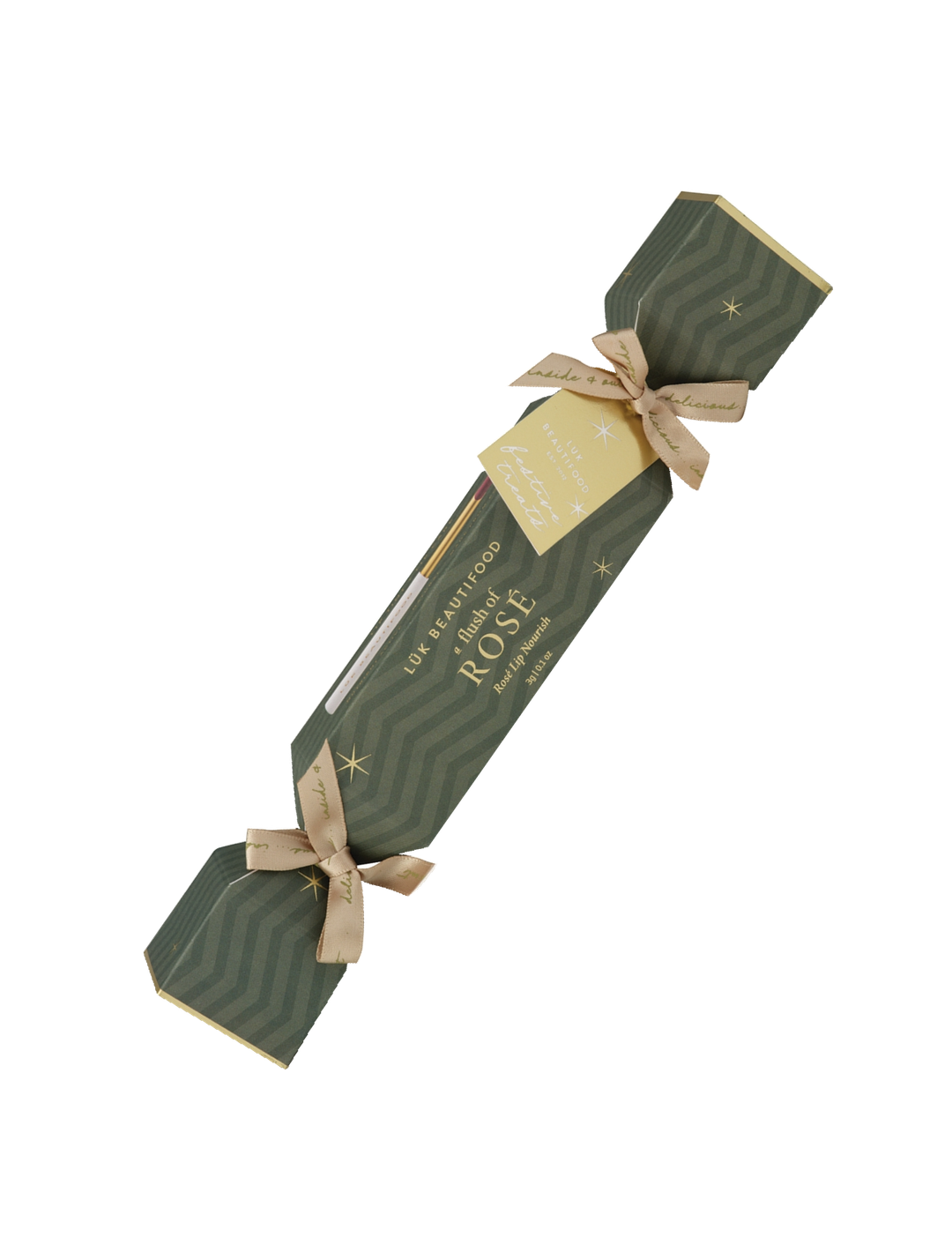 Single Luk Beautifood Rosé lip bonbon, a dark green patterned Christmas cracker with gold ribbon bows and a gift tag, shown diagonally on white. The packaging reads Flush of Rosé.