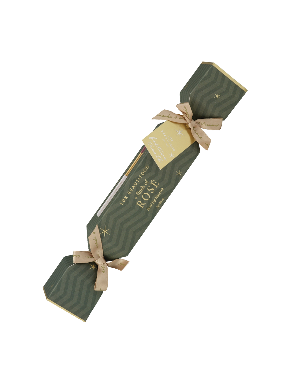 Single Luk Beautifood Rosé lip bonbon, a dark green patterned Christmas cracker with gold ribbon bows and a gift tag, shown diagonally on white. The packaging reads Flush of Rosé.