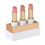 Luk Beautifood Lip Nourish Trio Sheer Delight, with three uncapped pink, bronze and nude shimmer lipsticks standing in a white presentation base with gold trim.