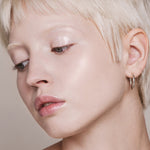Portrait of a woman with short platinum-blonde hair looking downward, with fair skin and light reflecting from her eyelid and cheekbone.
