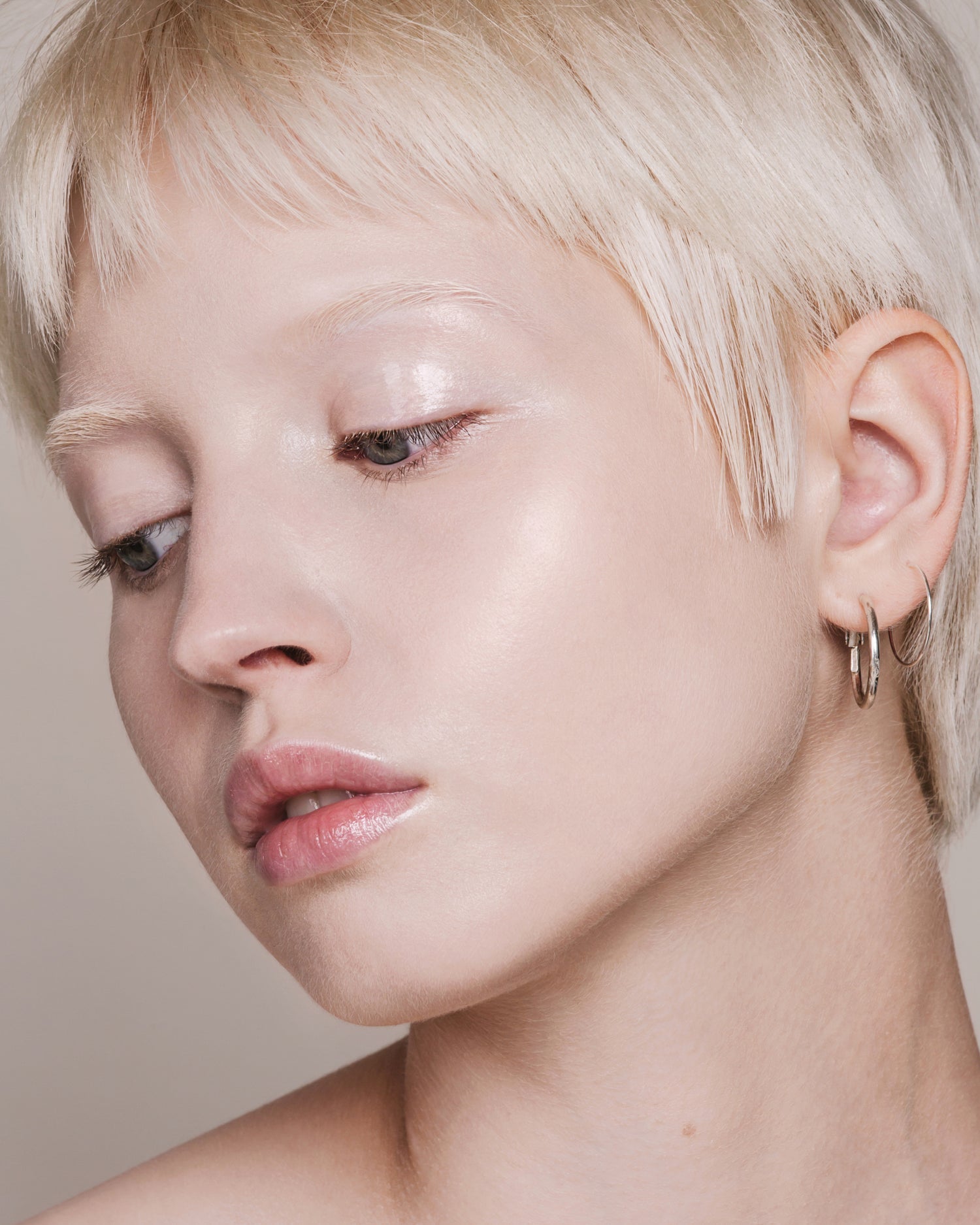 Portrait of a woman with short platinum-blonde hair looking downward, with fair skin and light reflecting from her eyelid and cheekbone.
