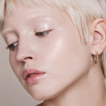 Portrait of a woman with short platinum-blonde hair looking downward, with fair skin and light reflecting from her eyelid and cheekbone.