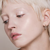 Portrait of a woman with short platinum-blonde hair looking downward, with fair skin and light reflecting from her eyelid and cheekbone.