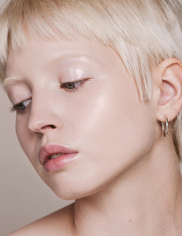Portrait of a woman with short platinum-blonde hair looking downward, with fair skin and light reflecting from her eyelid and cheekbone.
