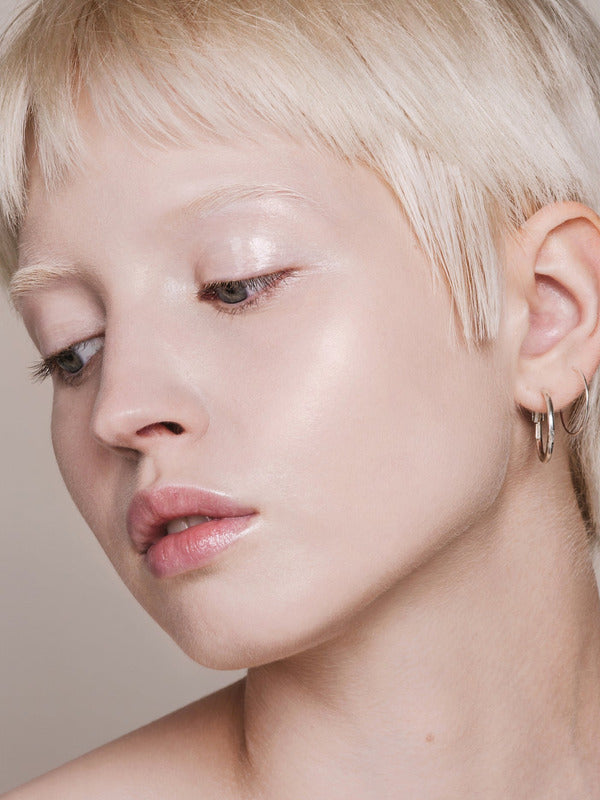 Portrait of a woman with short platinum-blonde hair looking downward, with fair skin and light reflecting from her eyelid and cheekbone.
