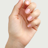 A hand with neatly manicured nails painted in Sienna Byron Bay Nail Polish - Magic, a soft, pale cherry blossom pink shade, is held up against a plain light background.
