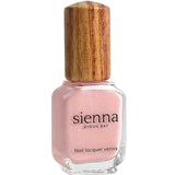 A bottle of Sienna Byron Bay Nail Polish - Magic, a cherry blossom pink shade with a light shimmery finish and wooden cap, crafted as toxin-free polish, shown against a white background.