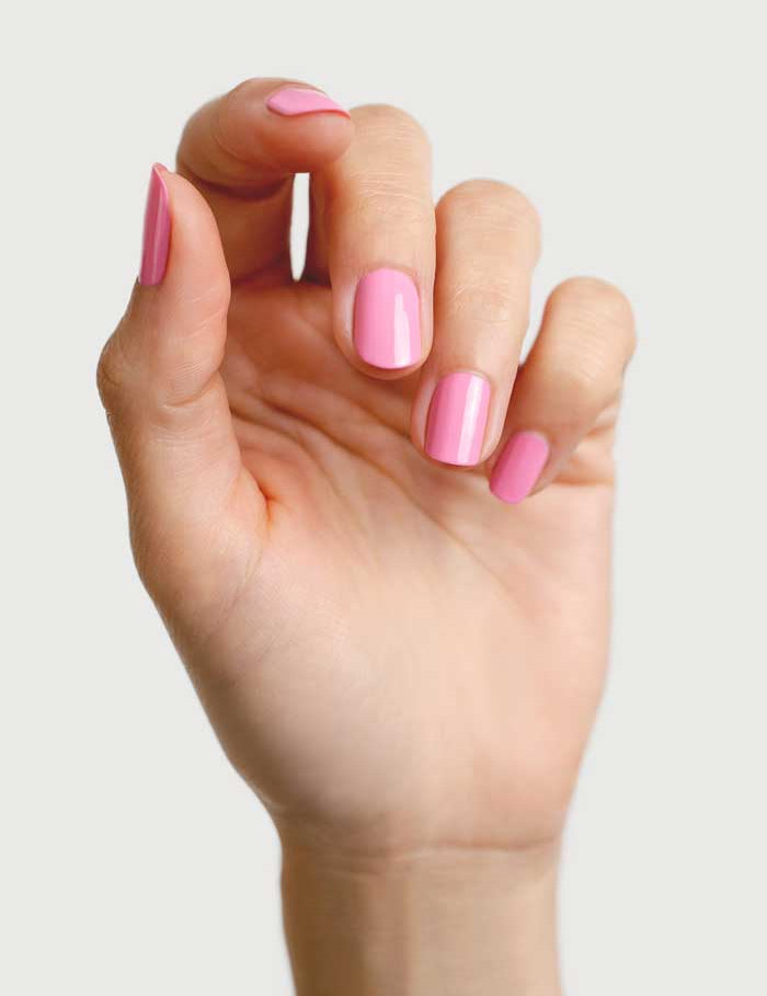A hand with neatly manicured nails painted in Sienna Byron Bay Nail Polish - Magnolia, a glossy, plant-derived pink shade, shown against a plain light background.