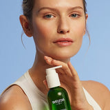 Young woman holding a bottle of Make-up Removal Cleansing Oil on a light blue background.