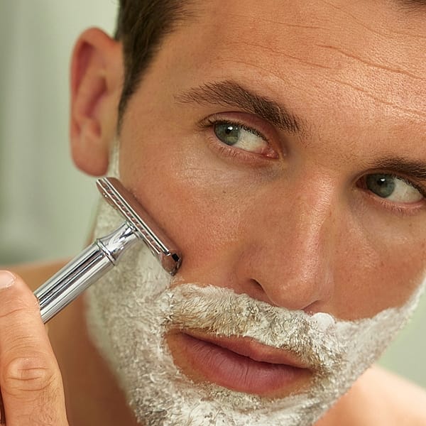 Man looking in the mirror with shaving cream on his face and holding a razor to his face.