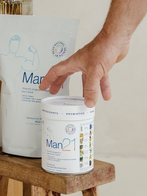Hand resting on a white Man21 tub on a small wooden stool, with a large matching refill pouch standing behind it.
