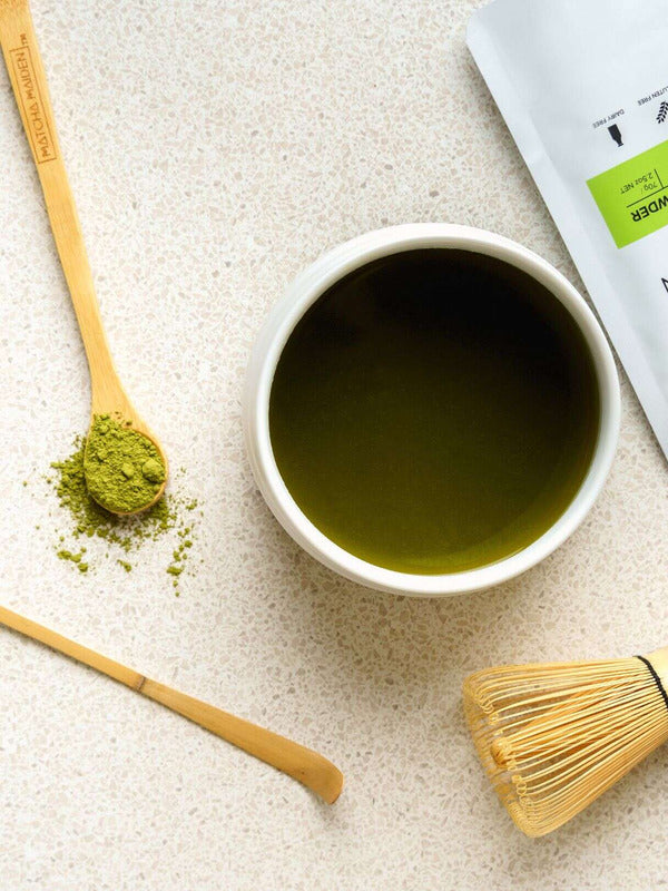 Matcha Maiden bamboo chasen whisk styled beside prepared matcha, matcha powder and bamboo tools.