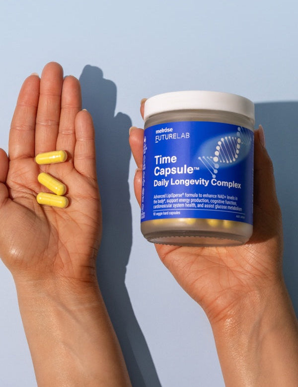 Hands holding Melrose FutureLab Time Capsule and daily capsules against a blue background