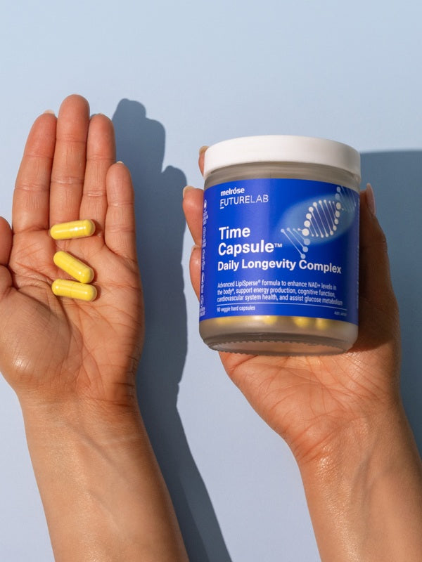 Hands holding Melrose FutureLab Time Capsule and daily capsules against a blue background