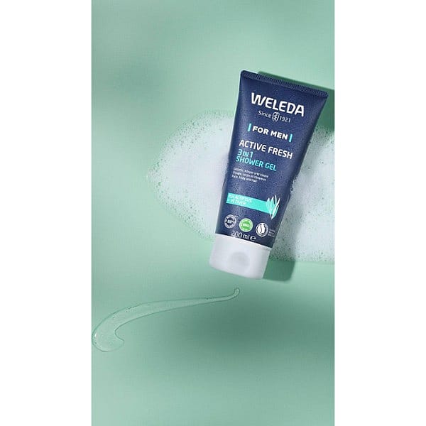 Tube of Weleda Men Active Fresh3-in-1 Shower Gel with eucalyptus and vetiver, surrounded by foam and gel on a light green background.