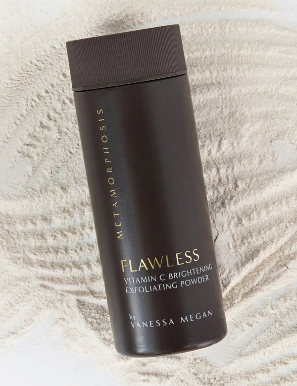 Tall dark brown Metamorphosis Flawless exfoliating-powder container with gold lettering lying diagonally over fine pale powder raked into curved ridges.