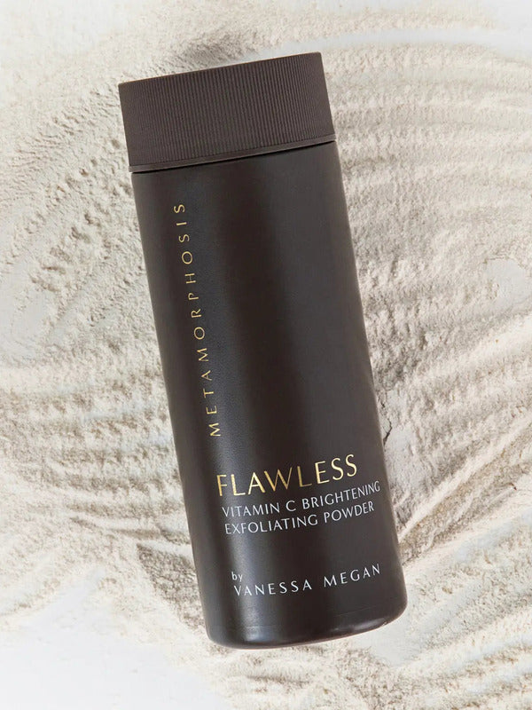 Tall dark brown Metamorphosis Flawless exfoliating-powder container with gold lettering lying diagonally over fine pale powder raked into curved ridges.