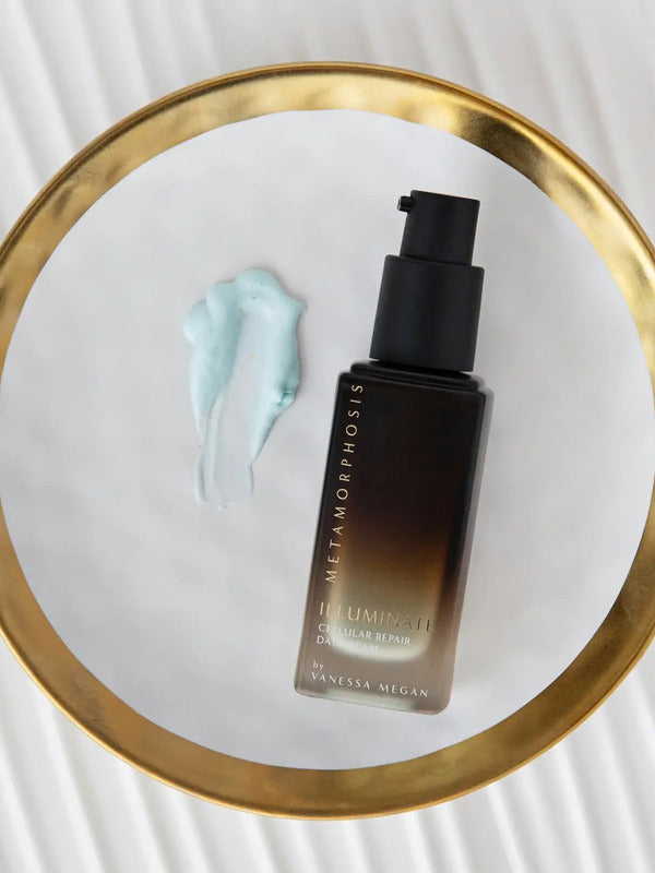 Dark amber Metamorphosis Illuminate pump bottle beside a pale blue cream smear on a round gold-rimmed mirror resting on a white ridged surface.