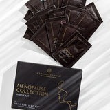 Black Metamorphosis Menopause Collection Starter Kit box below a fan of dark sample sachets on white marble with diagonal light and shadow.