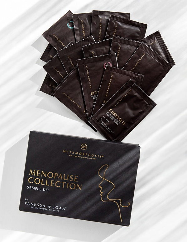 Black Metamorphosis Menopause Collection Starter Kit box below a fan of dark sample sachets on white marble with diagonal light and shadow.