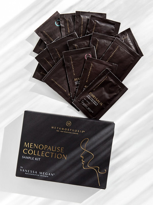 Black Metamorphosis Menopause Collection Starter Kit box below a fan of dark sample sachets on white marble with diagonal light and shadow.