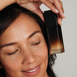 Woman holding Metamorphosis Peptide Amino Acid Serum beside her face with glowing skin.
