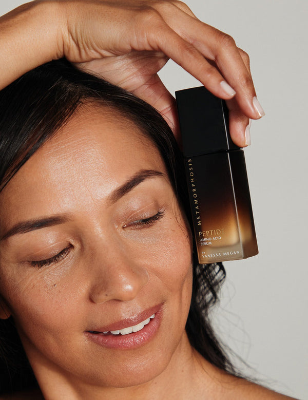 Woman holding Metamorphosis Peptide Amino Acid Serum beside her face with glowing skin.
